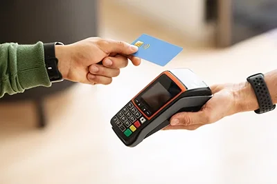 Customer in green sleeve holding blue contactless credit card over payment terminal held by store employee for tap-to-pay transaction