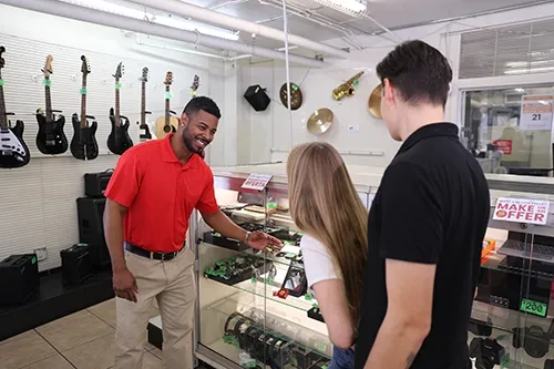 An employee in a modern pawn shop assisting customers while they are browsing merchandise. This represents a modern pawn shop interaction.